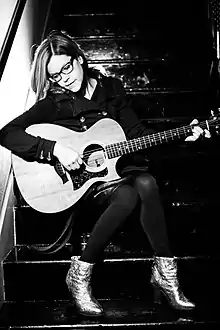 A black-and-white photo of Loeb seated in a stairwell, holding a guitar